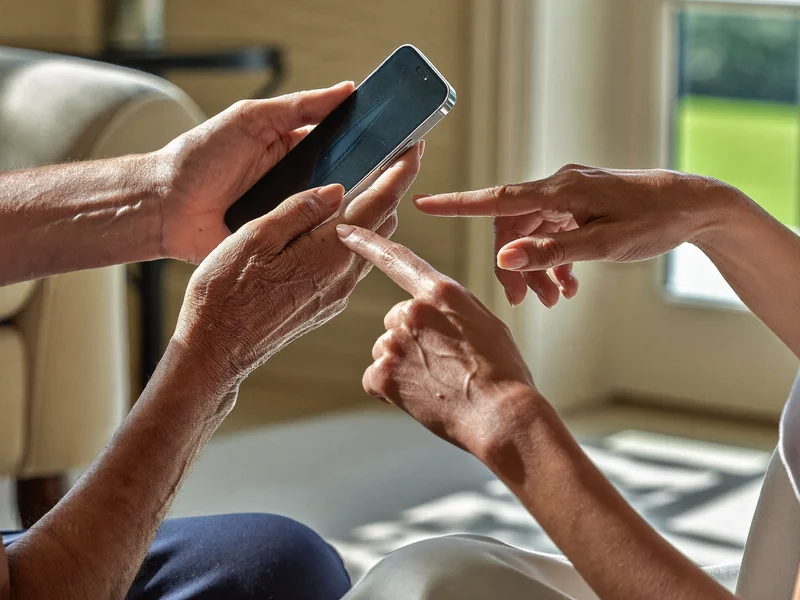 Le mani di un uomo anziano tengono lo smartphone mentre il tutor indica lo schermo